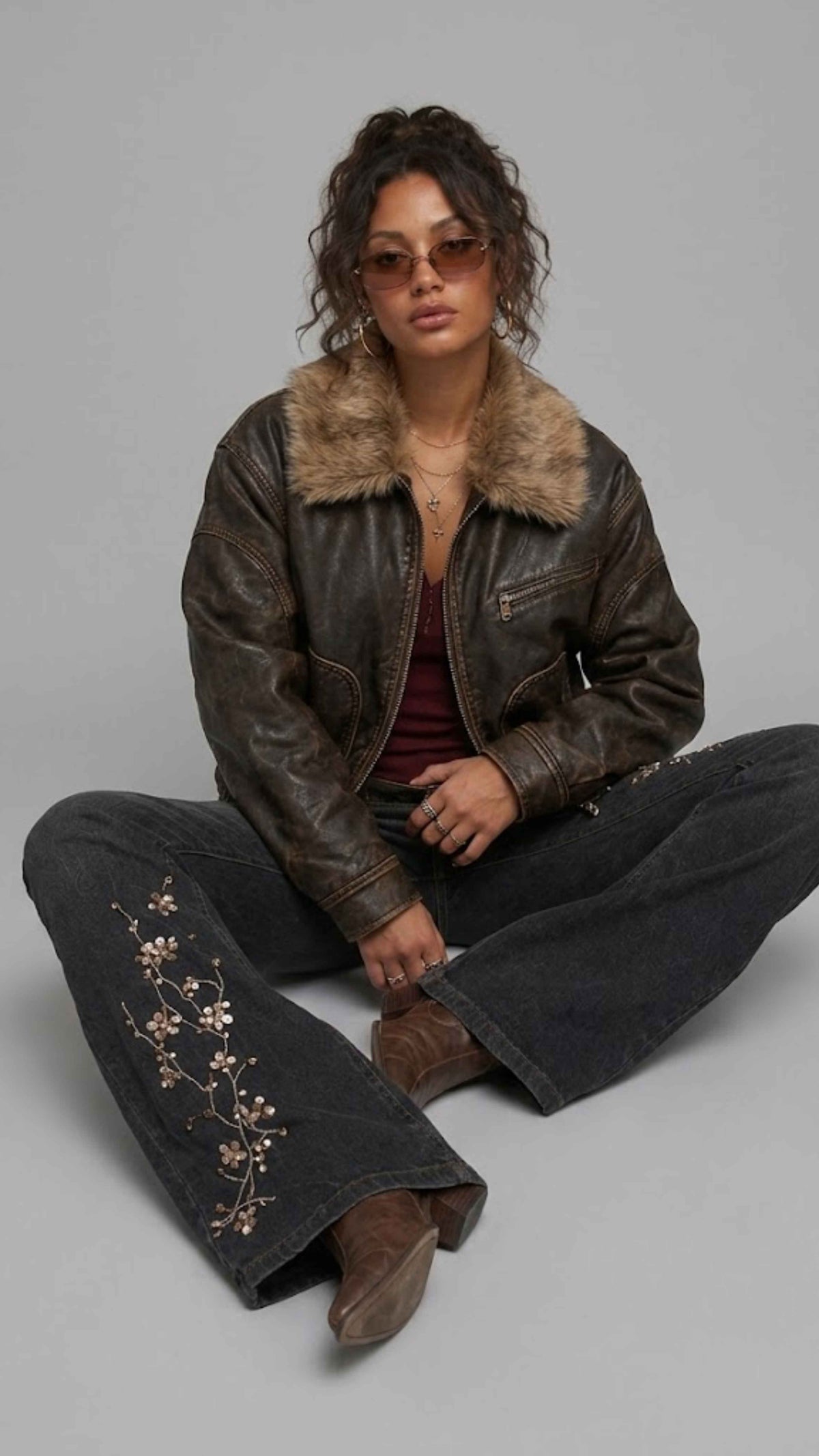 Urban grunge fashion presentation featuring a baggy distressed dark brown leather jacket accented with fur, styled for a vintage winter look.