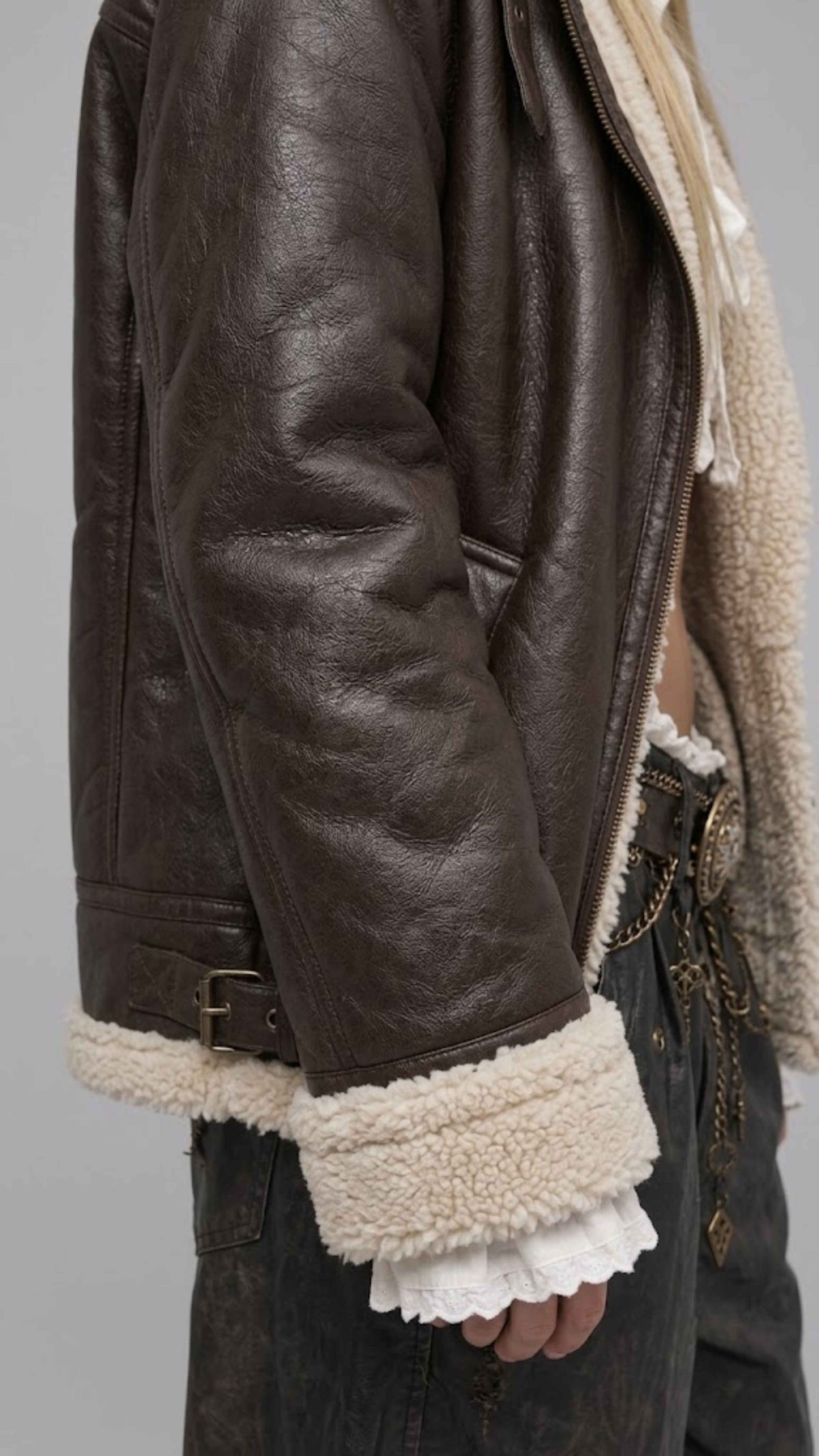 Detailed view of the slouchy oversized sleeve cuffs and waist hem on a dark chocolate leather coat accented with plush shearling trim.