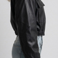 Close-up shot showing the smooth texture of high-quality black leather and precise stitching along the cropped waistband and cuffs.