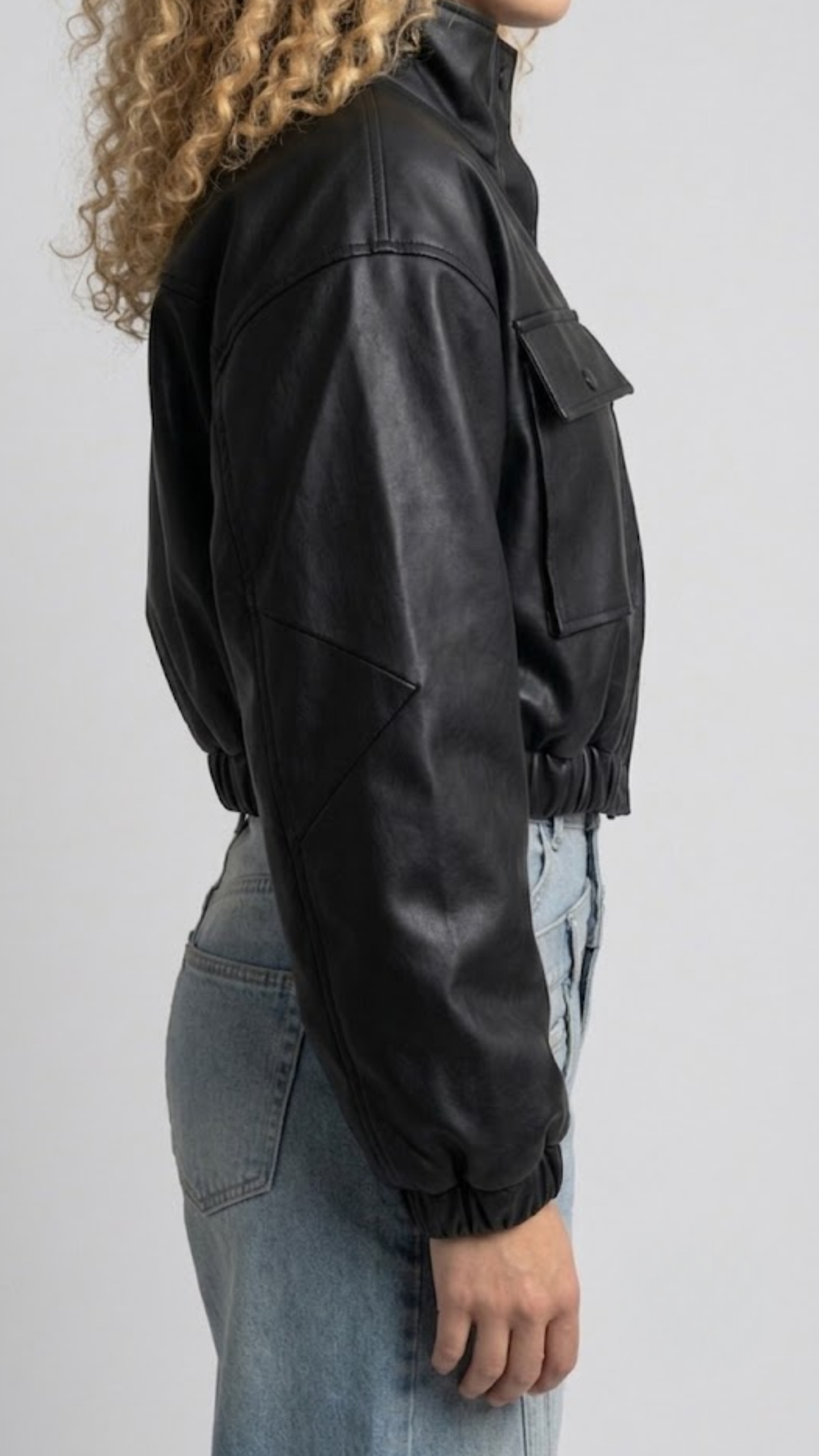 Close-up shot showing the smooth texture of high-quality black leather and precise stitching along the cropped waistband and cuffs.
