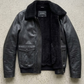 Jackero jacket flat lay photography of a high-end black leather flight jacket with shearling lining on a solid grey backdrop.