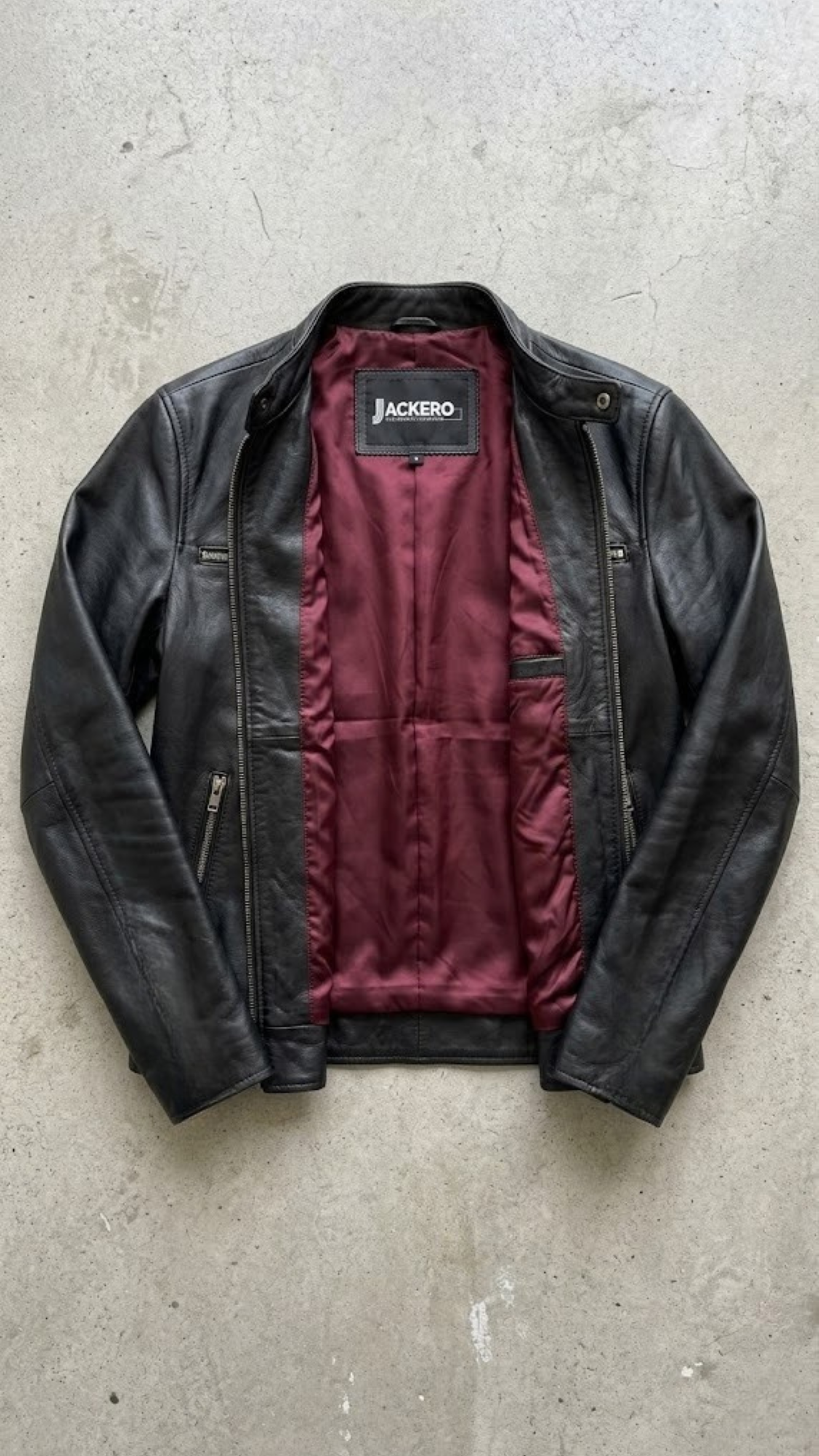 Jackero jacket flat lay photography of a high-end black leather motorcycle coat displayed symmetrically on a solid grey backdrop.