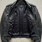 flat lay photography of a high-end vintage wash black leather café racer coat on a solid neutral backdrop.