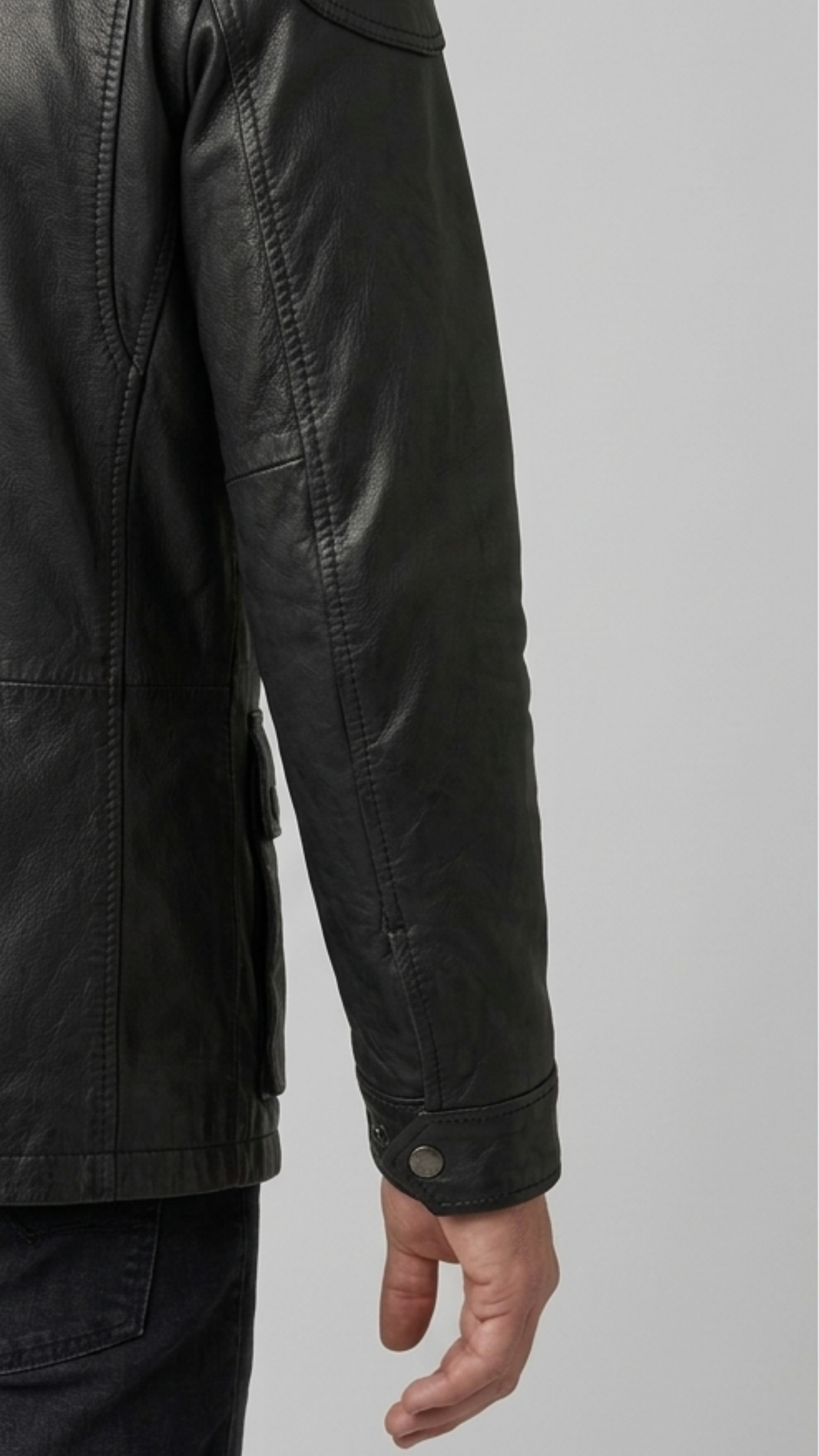 Close-up shot showing the rugged texture of high-quality black leather paired with durable metallic snap buttons on a field coat pocket.