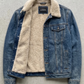 A dark gray washed denim jacket with a thick cream-colored sherpa lining, laid flat against a textured gray concrete background.