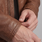 Close-up macro shot showcasing the rich natural grain, unique earthy undertones, and precise stitching on a premium brown genuine leather jacket.