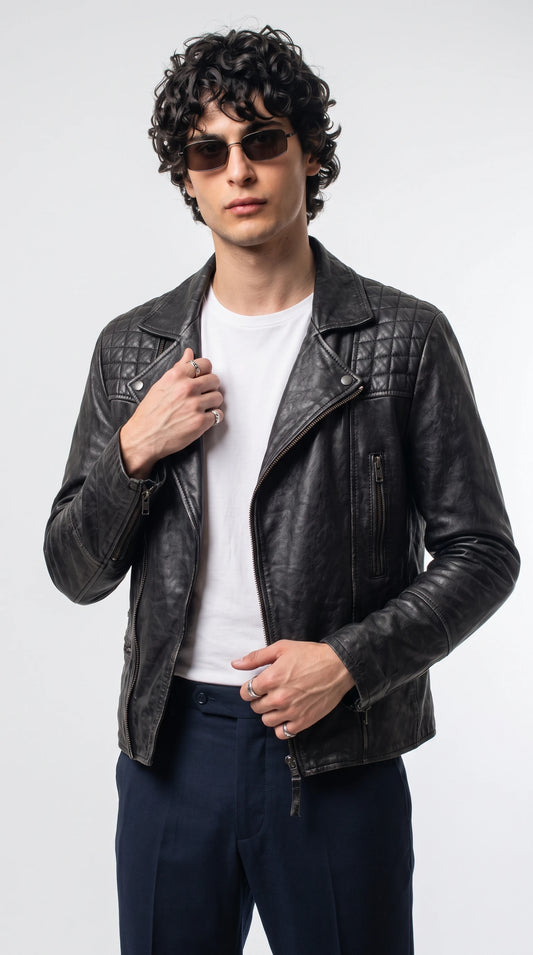 Jet-black genuine leather double-rider moto jacket with diamond-quilted shoulder panels, wide notched lapels, silver snap fasteners and an asymmetrical front zipper, styled with a white T-shirt and navy trousers for rebellious luxury streetwear.