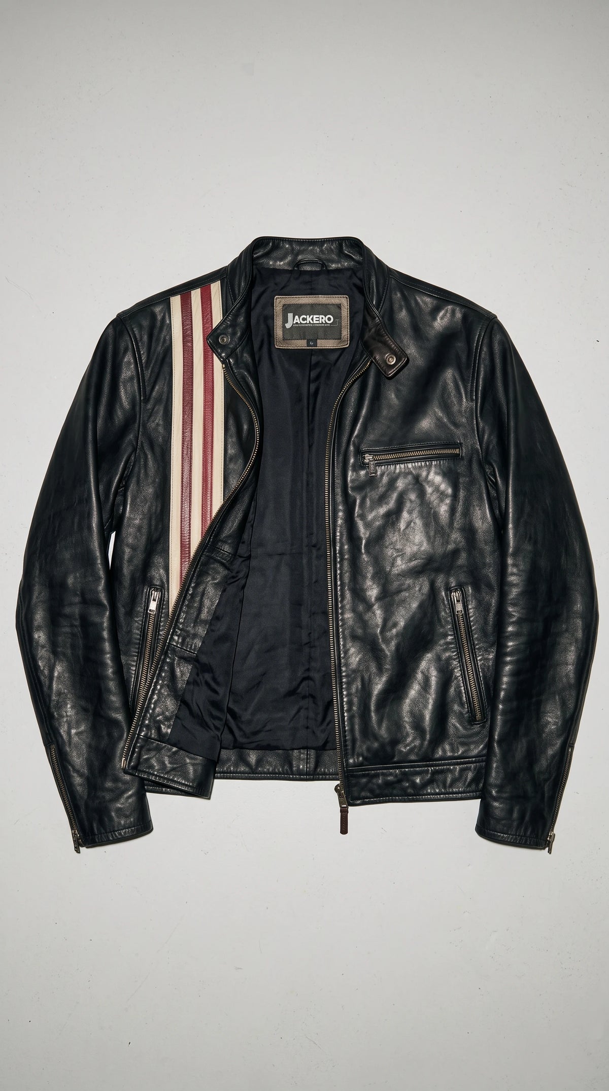 JACKERO black genuine leather jacket displayed open to reveal its smooth satin-finish lining and signature neck label, with cream-and-burgundy vertical racing stripes, a snap-button stand-up collar, full-length metal zipper and multiple secure outer pockets.