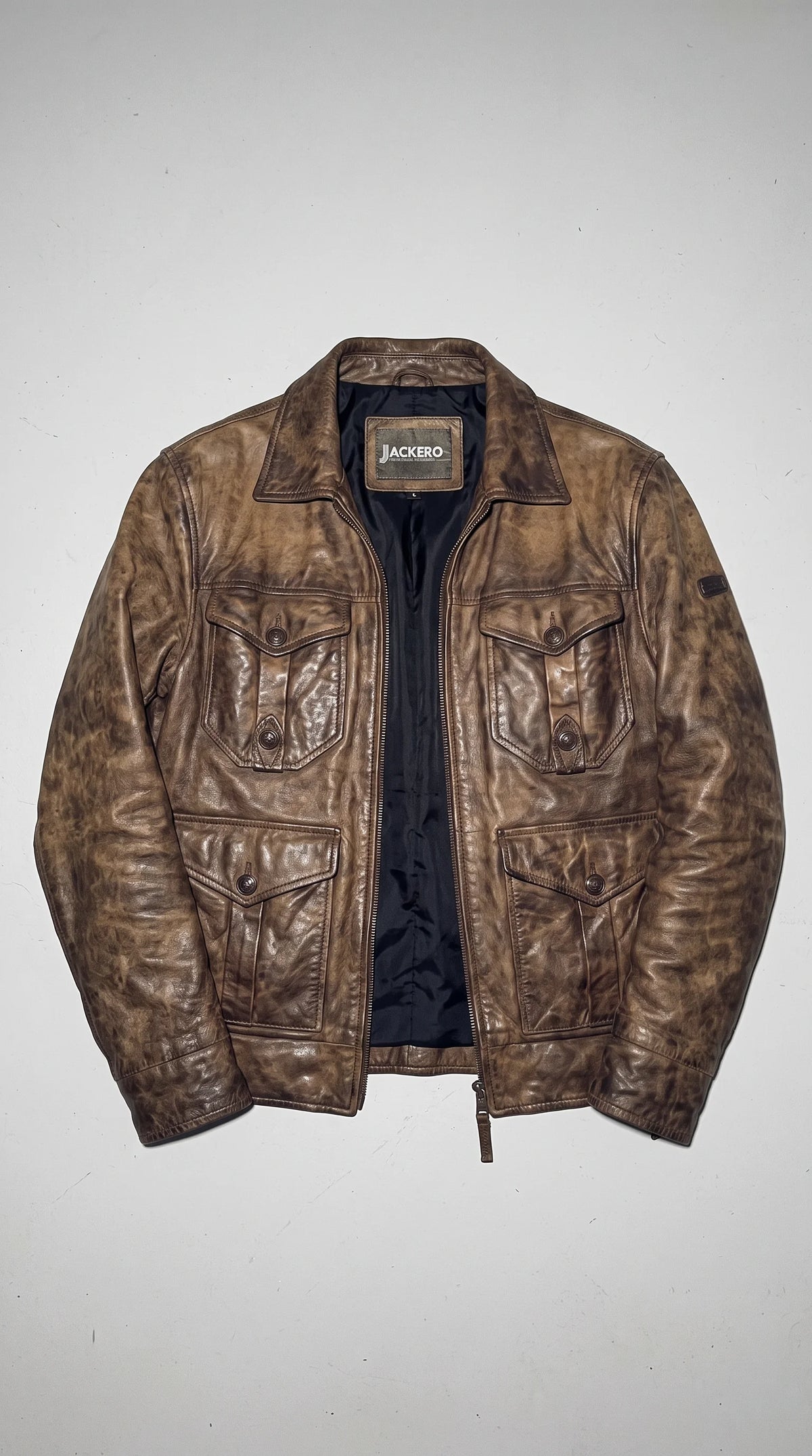 JACKERO distressed cognac-brown genuine leather field jacket with a shearling-lined fold-down collar, four functional button-flap pockets and a concealed zip fastening, bringing heritage workwear character to modern winter layering and understated premium streetwear.