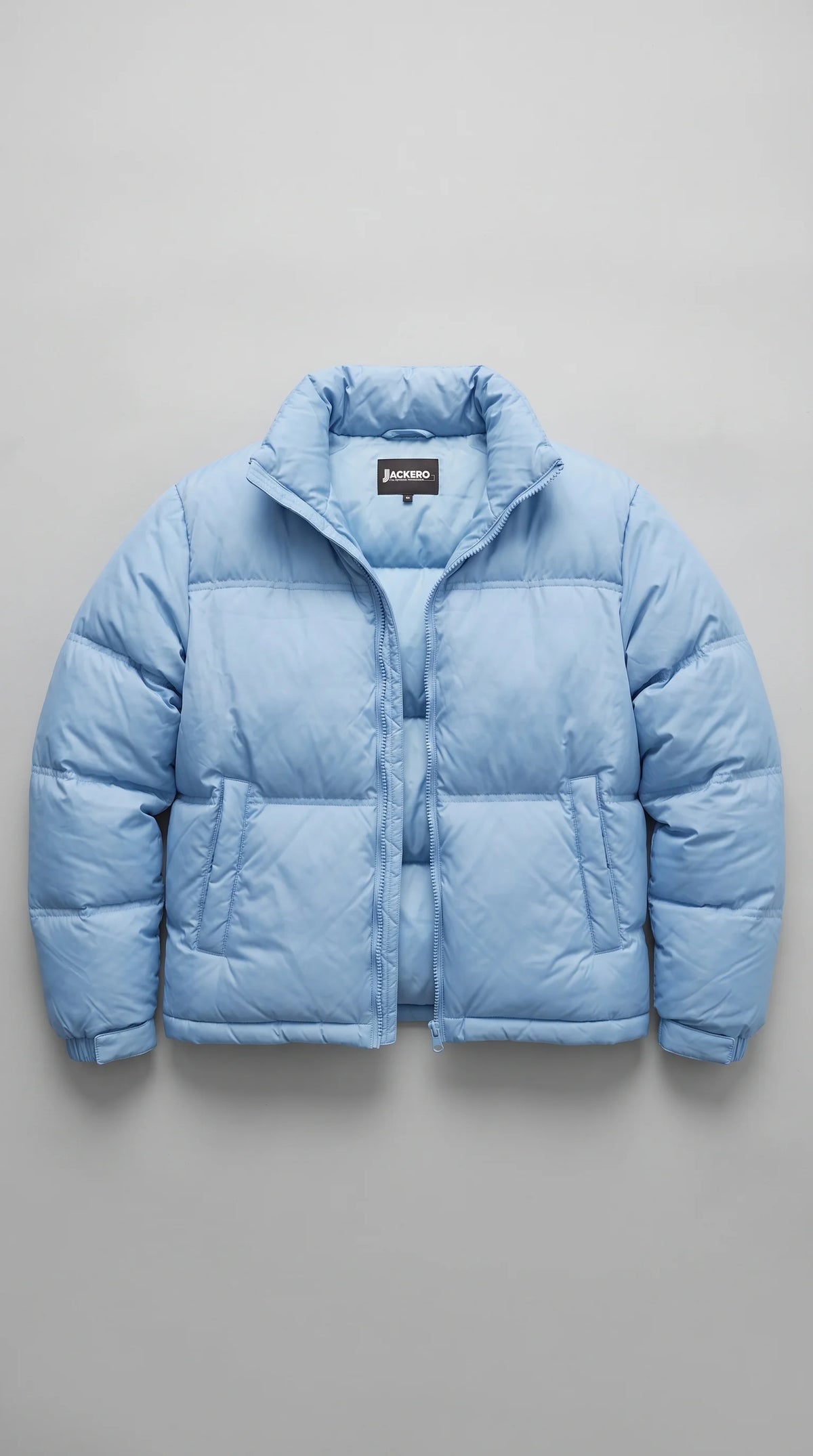 A light blue puffer jacket with a high collar and front zipper, laid flat against a neutral gray background. The brand label 'JACKERO' is visible inside the collar.