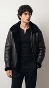 Jet black genuine leather aviator jacket with an oversized plush black faux-shearling collar, exposed fluffy front trim and polished metal zipper, paired with an all-black outfit for a bold monochrome winter streetwear look.