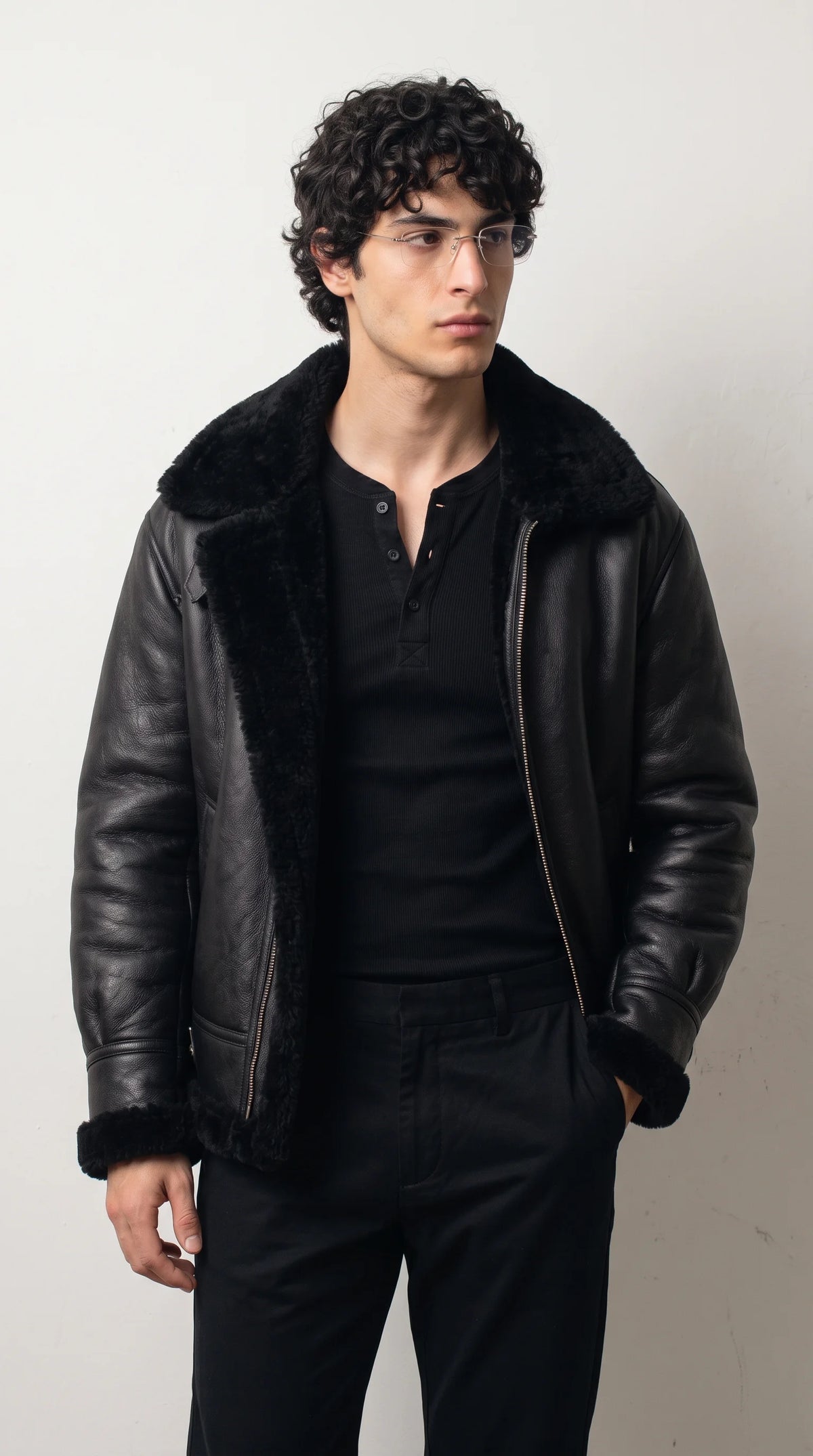 Jet black genuine leather aviator jacket with an oversized plush black faux-shearling collar, exposed fluffy front trim and polished metal zipper, paired with an all-black outfit for a bold monochrome winter streetwear look.