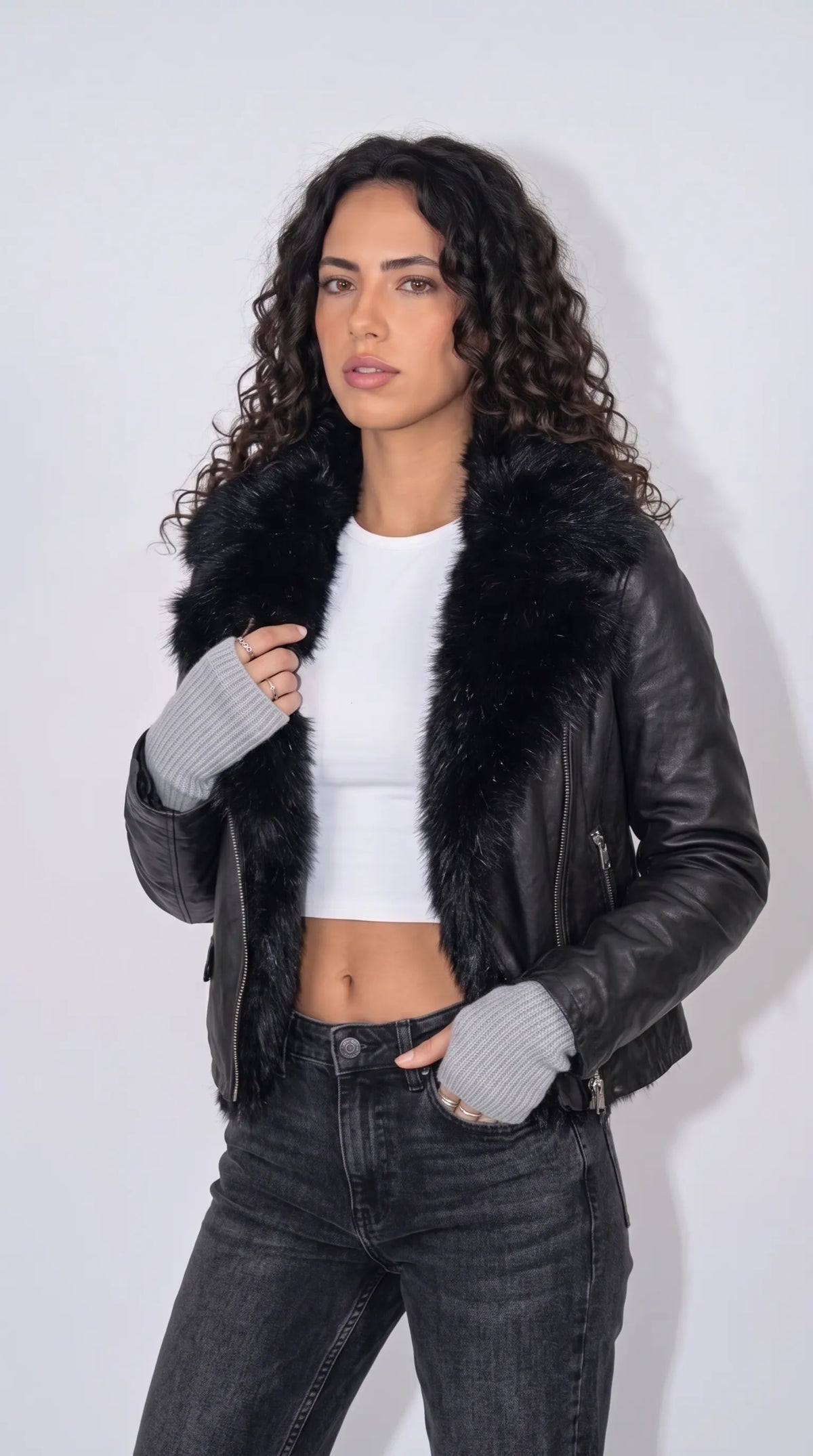 Jet-black genuine leather biker jacket with oversized plush black faux-fur lapels, an asymmetrical silver-tone zipper, vertical zippered pockets and polished zip cuffs, styled with a white fitted crop top and charcoal distressed jeans for bold monochrome streetwear.