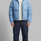 Front view of a model wearing a stylish light blue puffer jacket with quilted patterns, standing against a clean grey studio backdrop