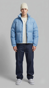 Front view of a model wearing a stylish light blue puffer jacket with quilted patterns, standing against a clean grey studio backdrop