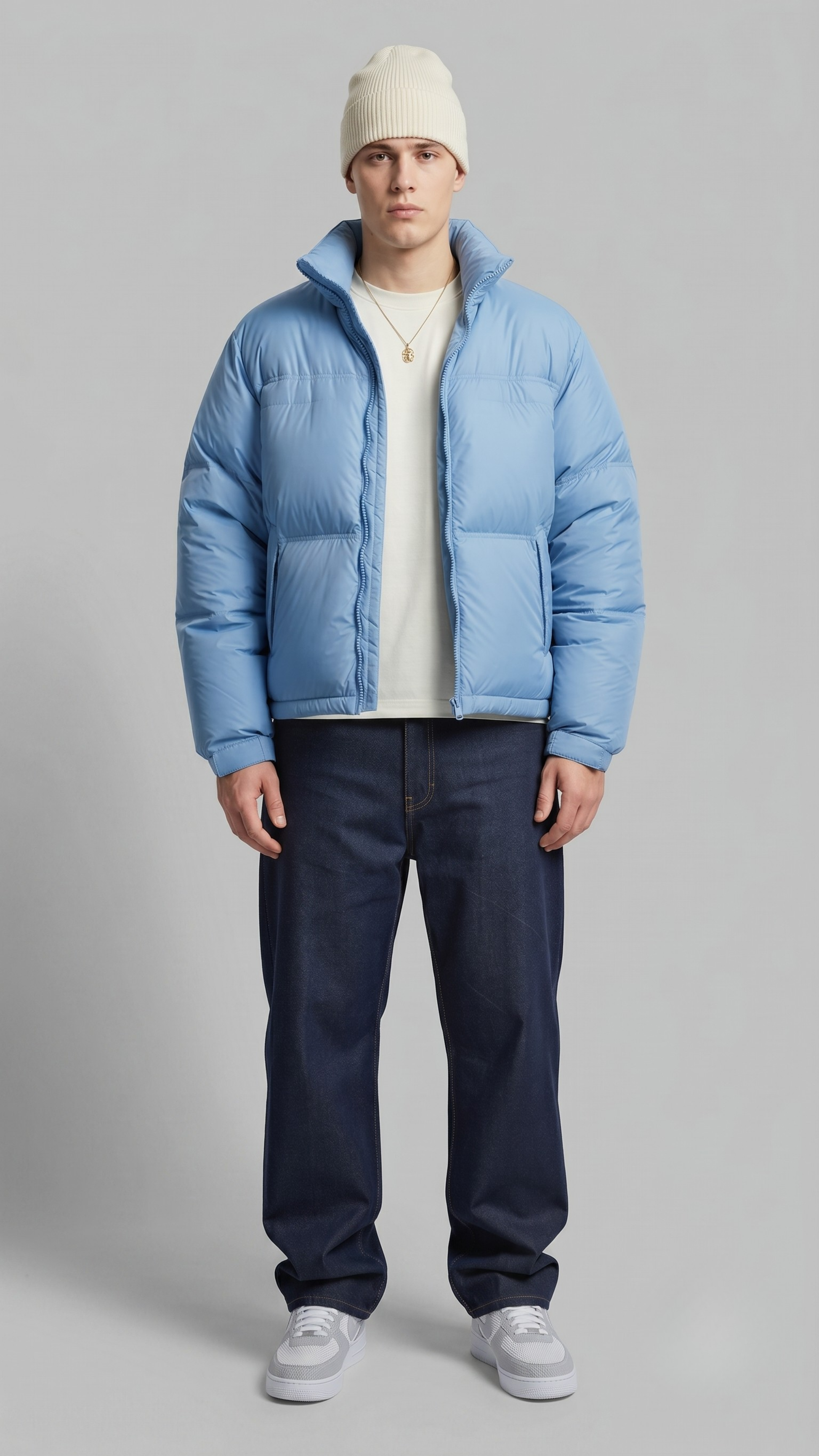 Front view of a model wearing a stylish light blue puffer jacket with quilted patterns, standing against a clean grey studio backdrop