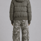 Rear view of loose fit olive puffer coat displaying broad horizontal quilted baffling and voluminous fur-trimmed hood