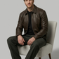 Man wearing a brown leather jacket sitting on a chair against a plain background