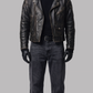 Man wearing a black leather jacket, black turtleneck, jeans, and gloves on a gray background