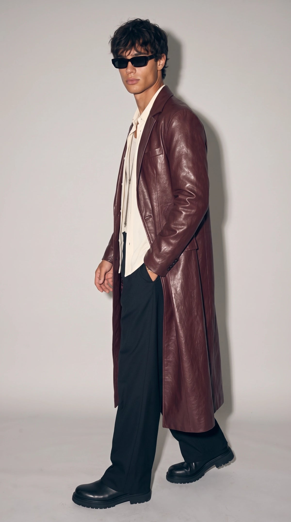 Men’s burgundy leather overcoat styled open over an ivory shirt and fine-knit mesh vest, with wide black trousers and chunky black shoes. Its classic notch lapels, long structured cut and rich dark-red finish bring a sophisticated old-money-inspired feel to contemporary city fashion, creating a striking outfit for evening events, elevated casual wear and modern street style.