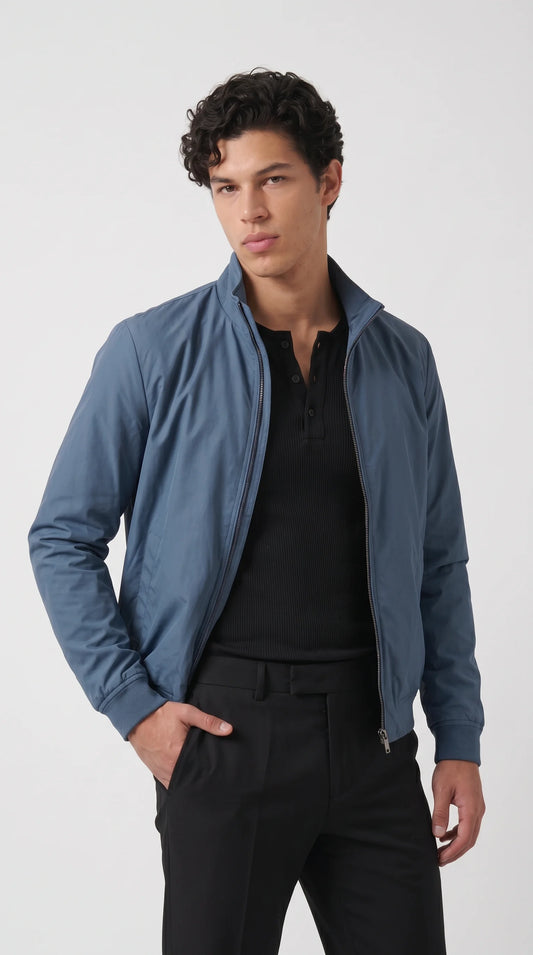 Men’s cyan-blue silk-cotton bomber jacket styled with a black ribbed shirt and tailored black trousers for a clean, contemporary city outfit. The smooth fabric, understated sheen, raised stand collar and streamlined zip-front design give this lightweight casual jacket a refined appearance, ideal for modern streetwear and smart everyday layering.