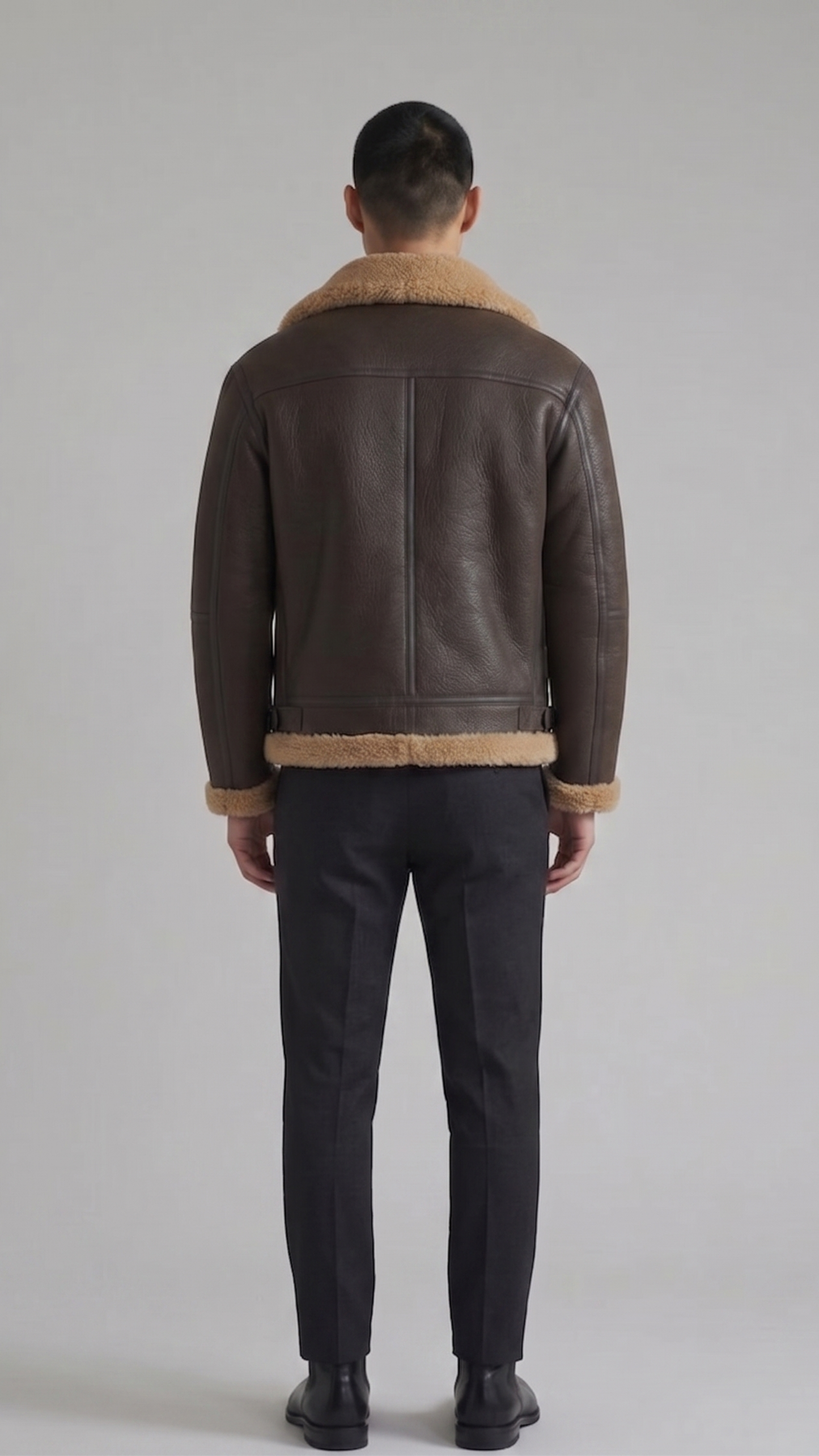 Man wearing a brown leather jacket with beige fur lining on a plain background
