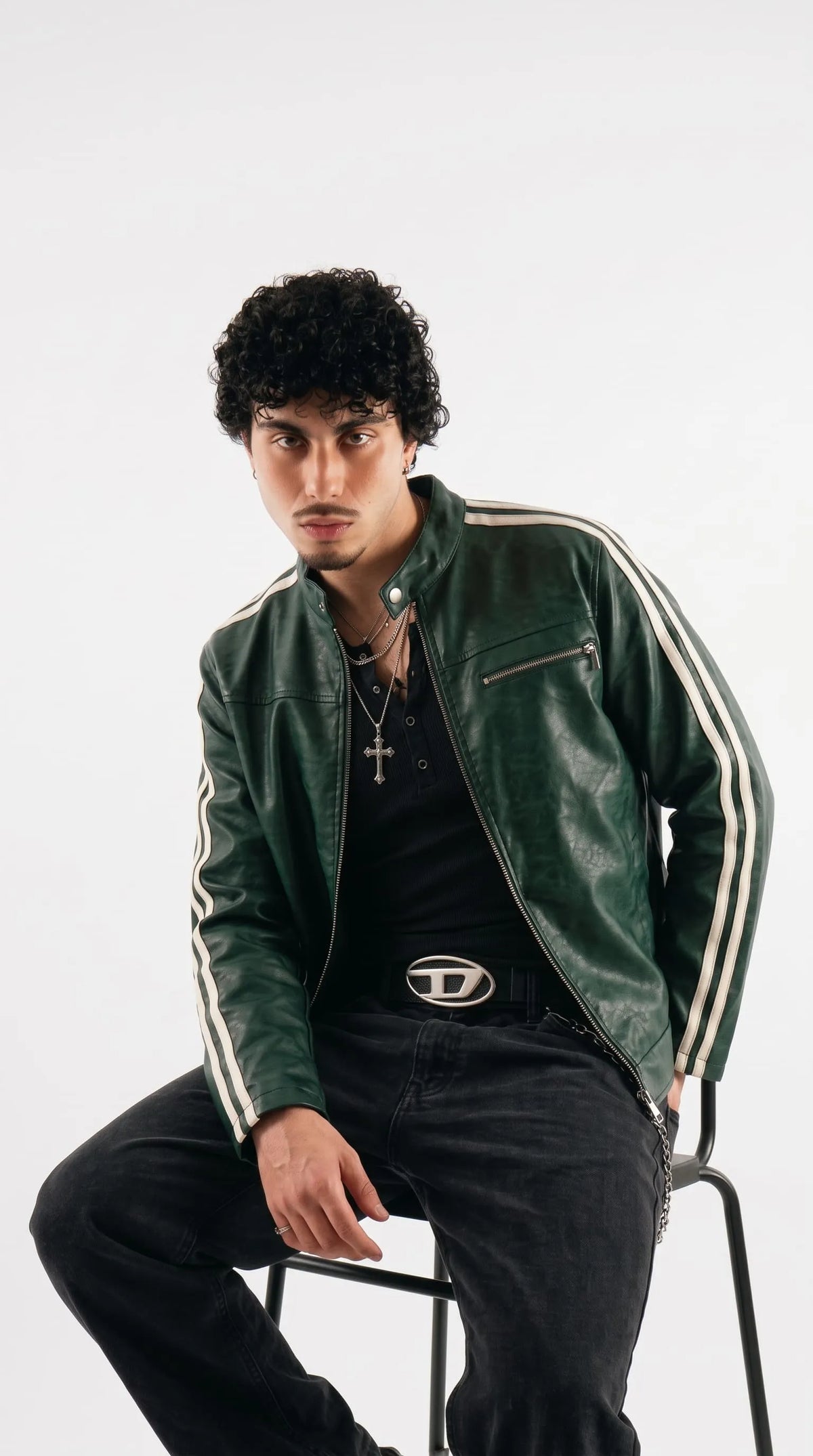 Seated model wearing a men's dark green leather cafe racer jacket with white sleeve stripes and a zip front.


