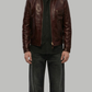 A male model wearing a dark brown leather jacket over a black shirt and dark gray jeans, standing against a solid gray background.