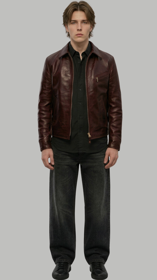 A male model wearing a dark brown leather jacket over a black shirt and dark gray jeans, standing against a solid gray background.