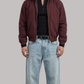 Man wearing a maroon jacket, black shirt, and light blue jeans on a gray background