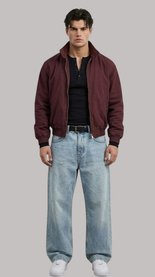 Man wearing a maroon jacket, black shirt, and light blue jeans on a gray background