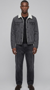 A man modeling a dark gray washed denim jacket with a white sherpa collar, worn over a black t-shirt and dark gray jeans, against a solid light gray background.