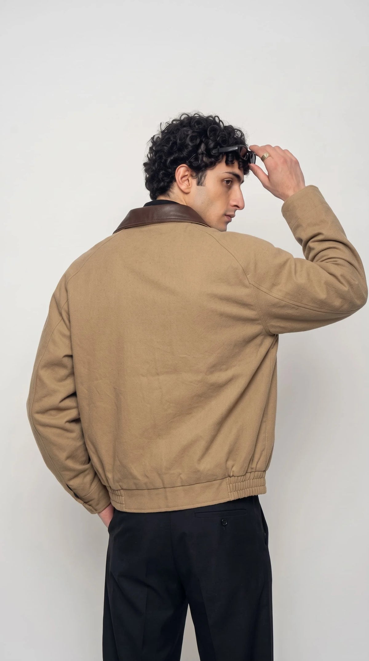 Model wearing an oversized beige bomber jacket with black wide-leg pleated trousers against a white studio background