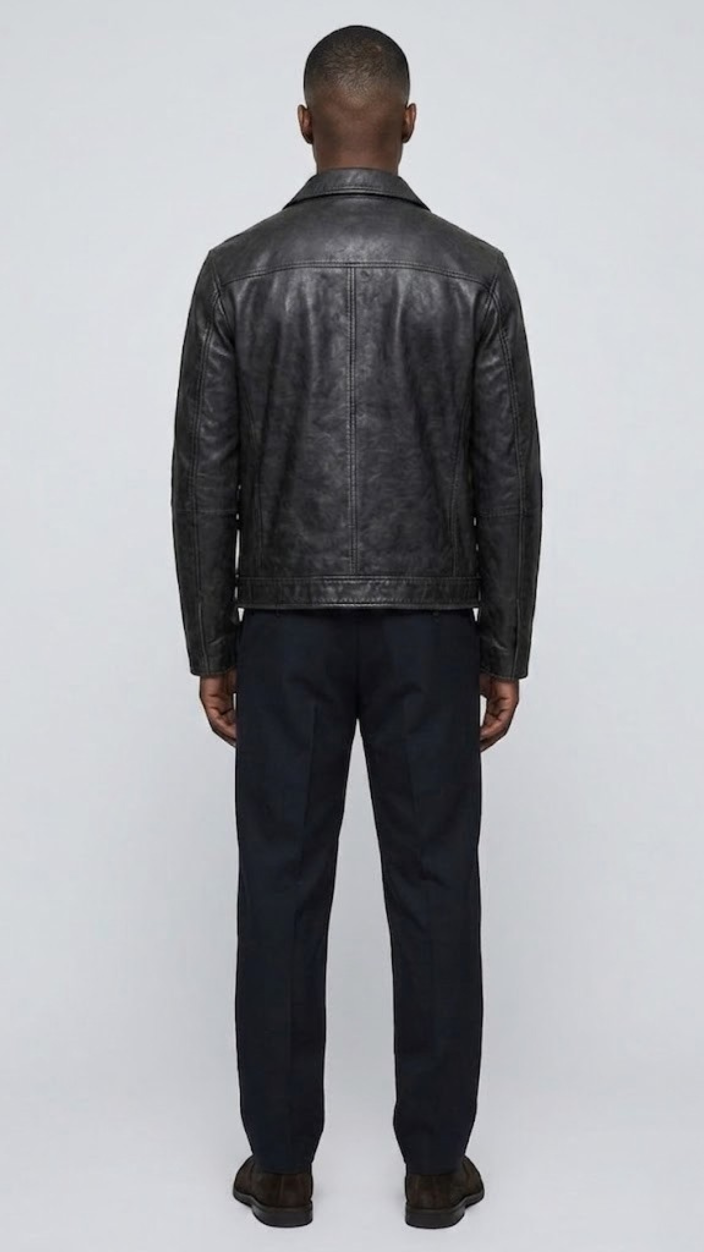 Straight-on back view of a structured plain black leather jacket highlighting its smooth surface, precise panel lines, and fitted silhouette.