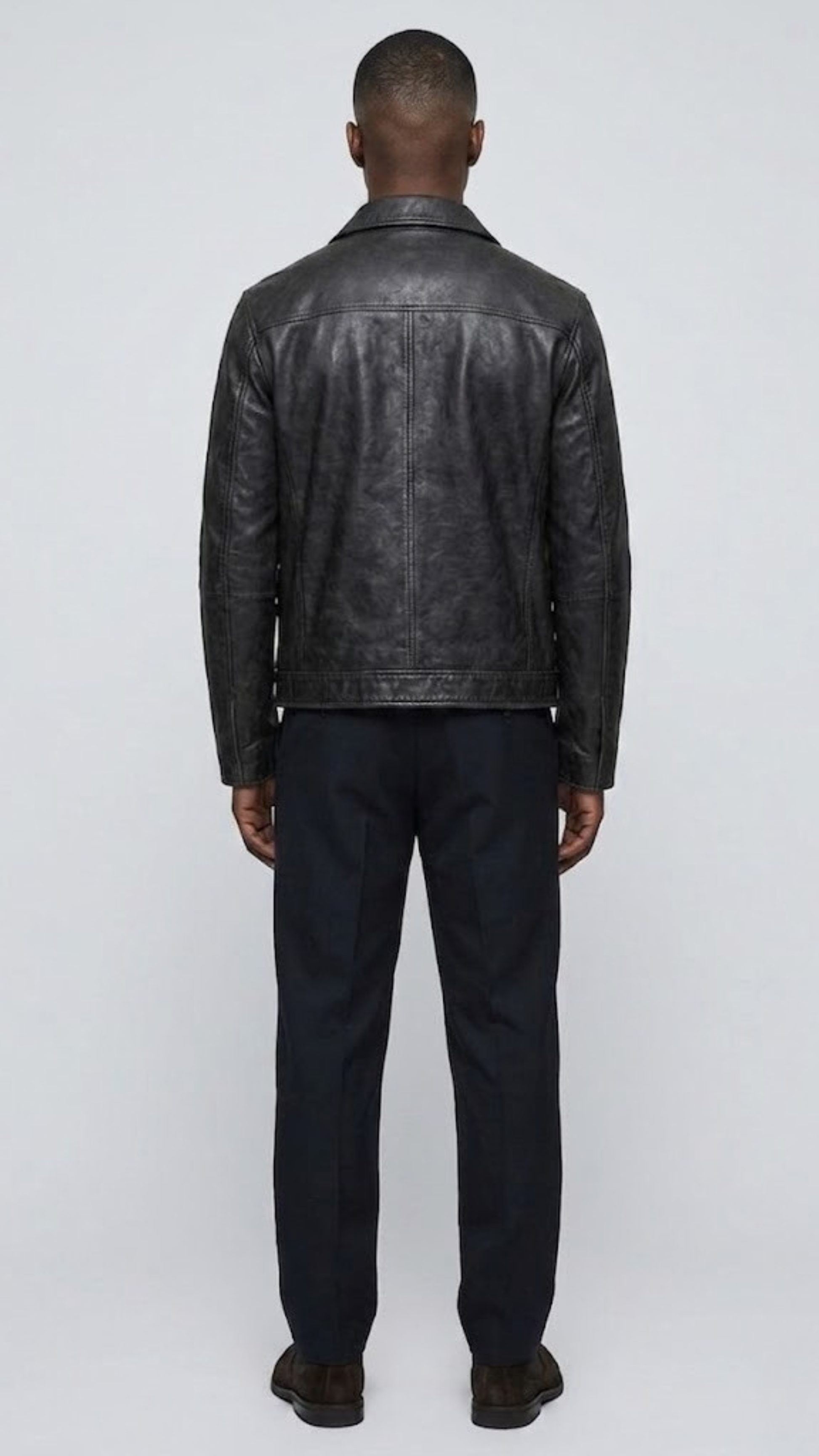 Straight-on back view of a structured plain black leather jacket highlighting its smooth surface, precise panel lines, and fitted silhouette.