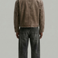 Person wearing a brown corduroy jacket and dark jeans on a plain background