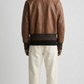 Symmetrical rear view studio shot highlighting the smooth streamlined paneling and sleek shoulder construction of the walnut brown leather coat.