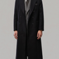 Model wearing a premium black double-breasted long wool coat standing in a studio setting.
