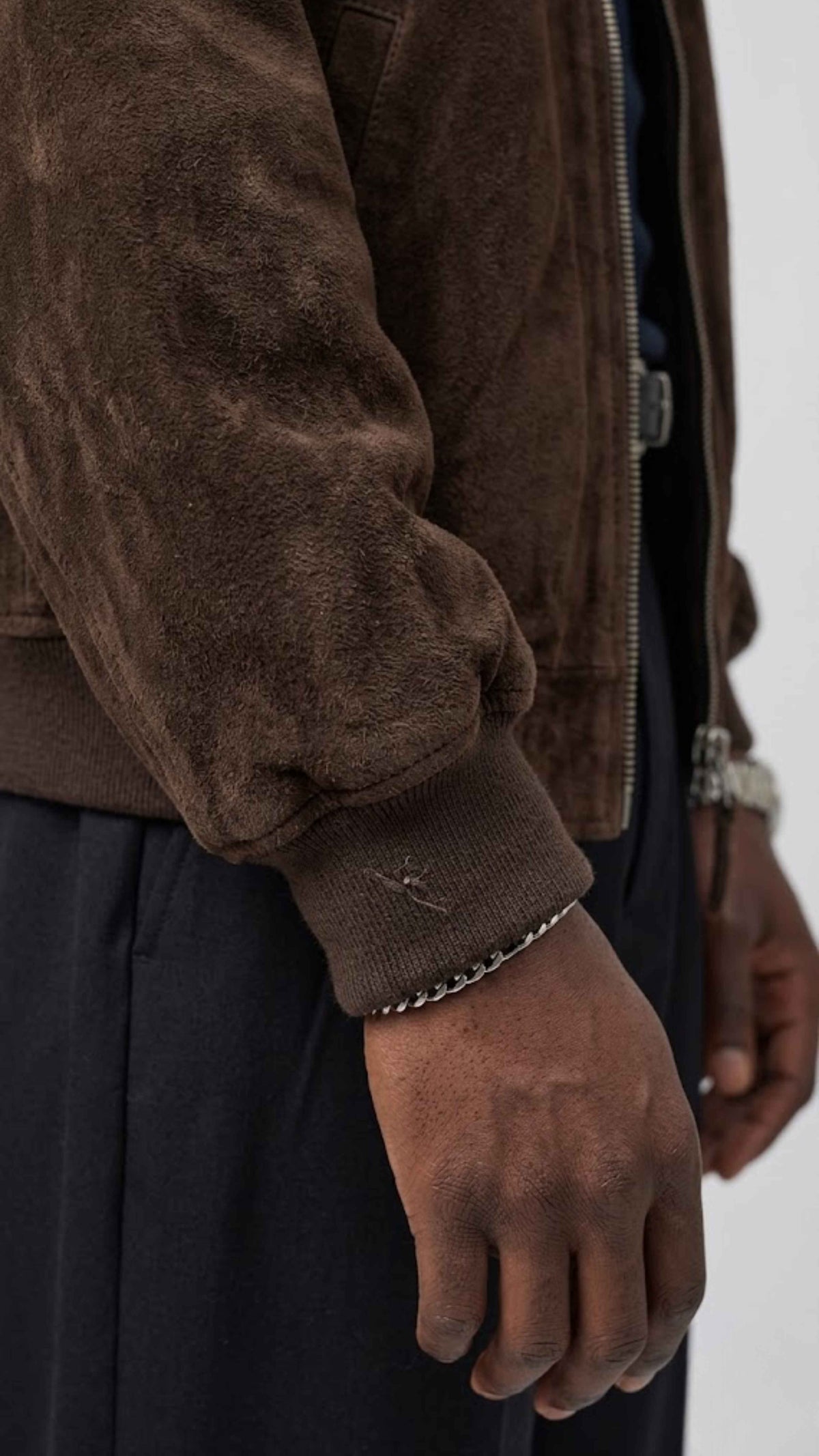 Detailed view of the structured minimal collar, metallic zipper closure, and deep side welt pockets on a dark brown suede coat.