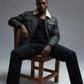 Symmetrical studio layout of a high-quality men's black leather trucker outerwear on a light grey backdrop.