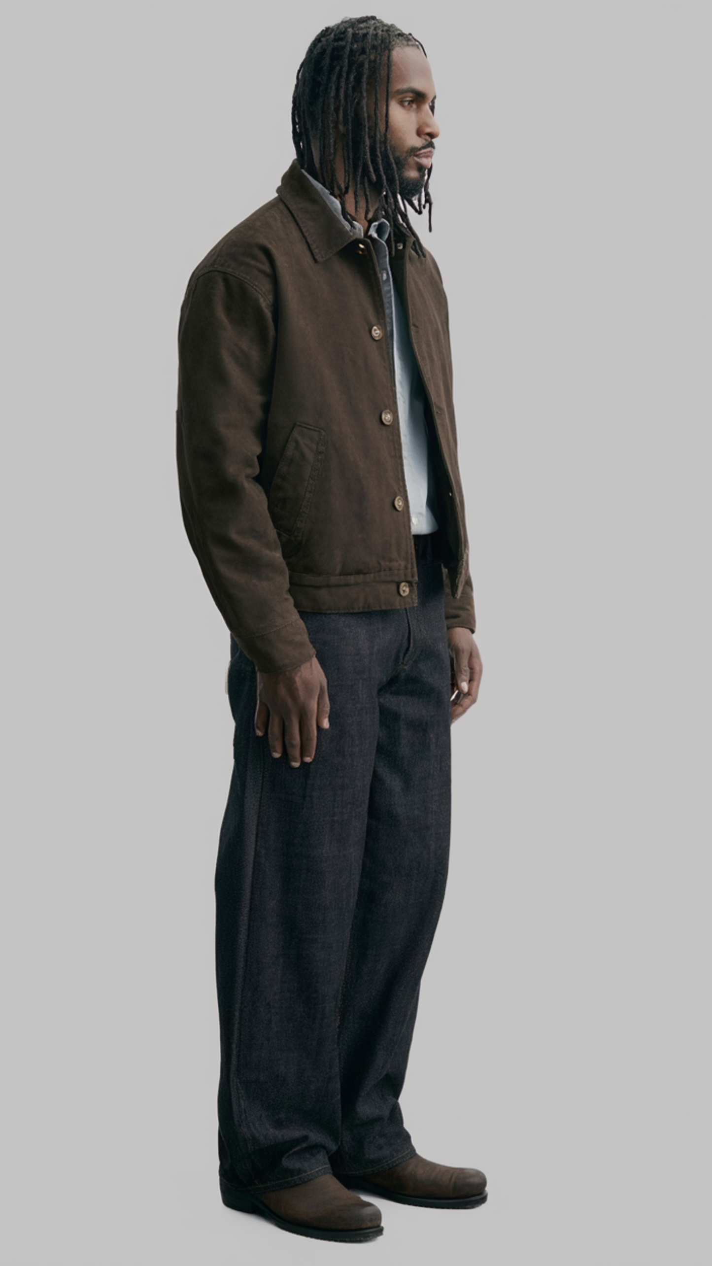 Man wearing a brown canvas jacket and dark pants on a gray background