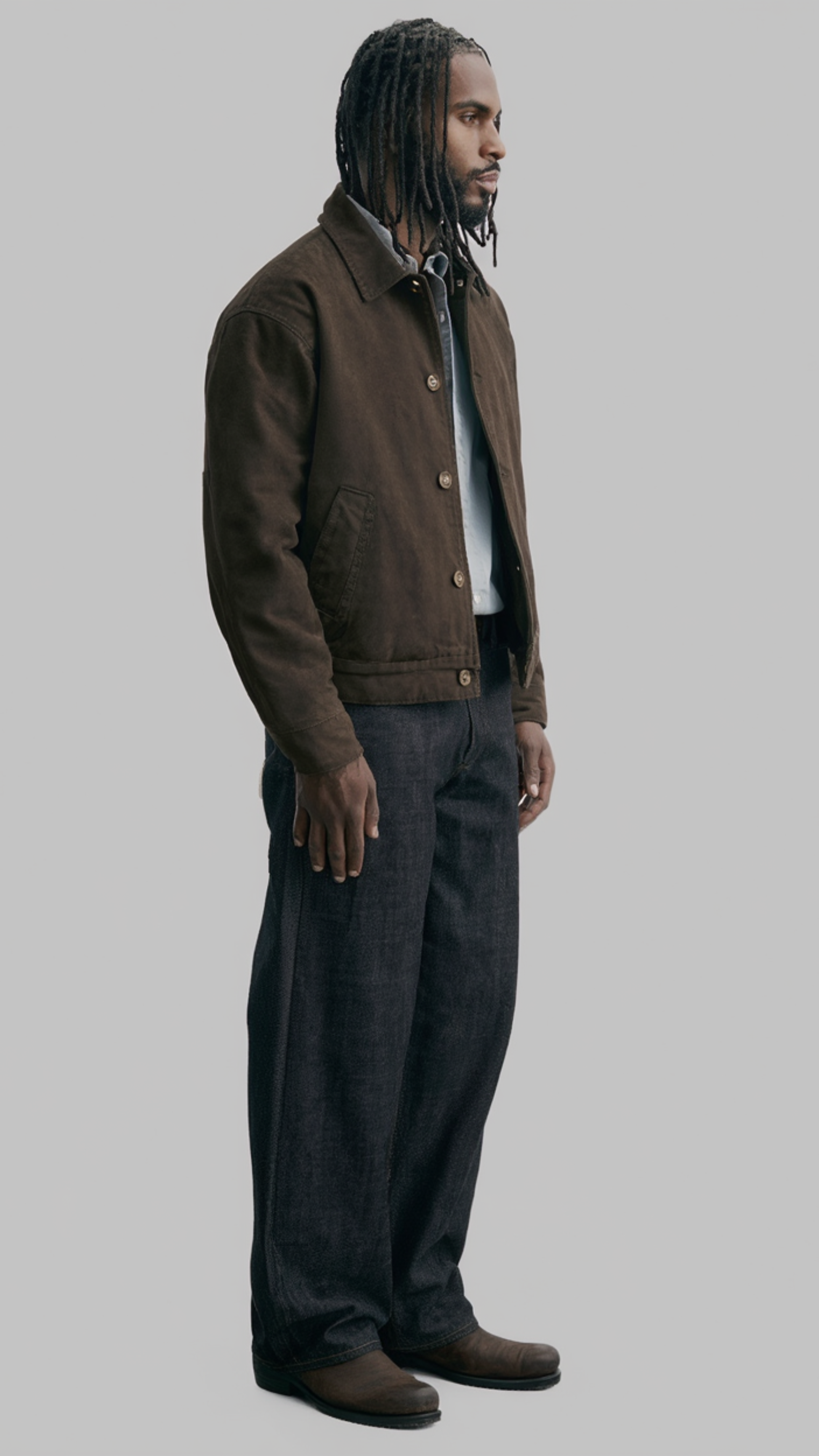 Man wearing a brown canvas jacket and dark pants on a gray background