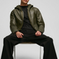 Man sitting on a chair wearing a green leather jacket and black pants against a white background