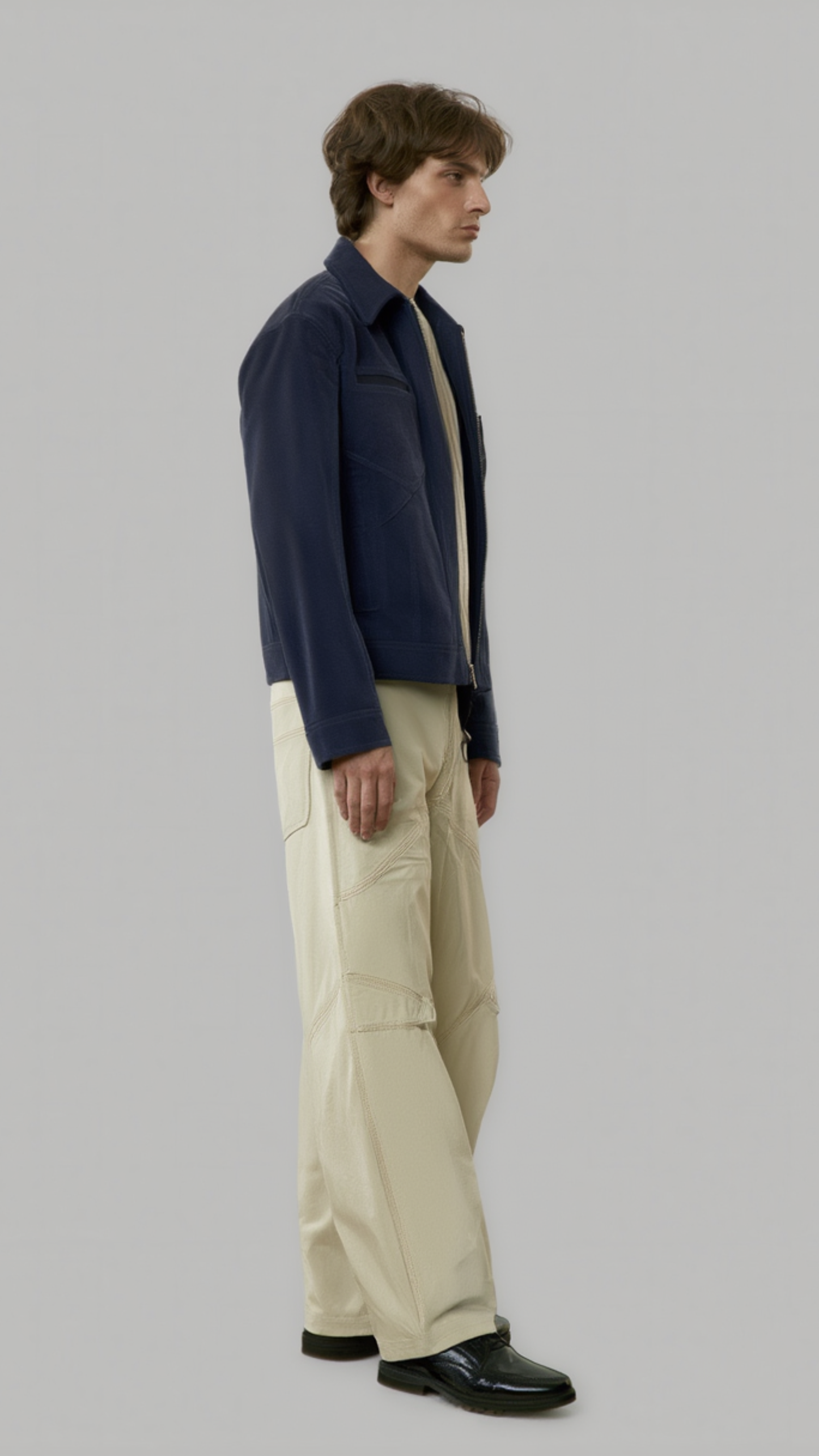 Man wearing a navy suede bomber jacket and beige pants on a gray background