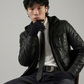 Man wearing a black leather jacket and gloves sitting on a chair against a gray background