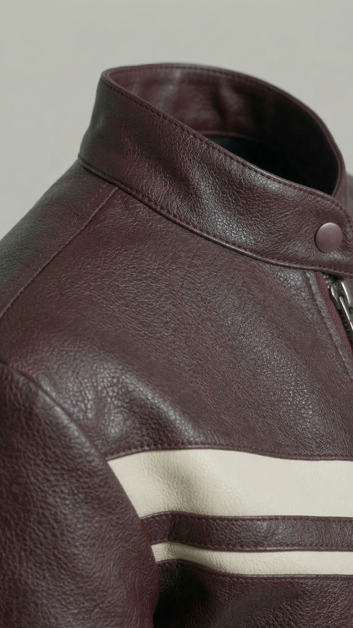 Close-up of a dark brown leather jacket with a high collar and a horizontal cream stripe across the chest.