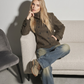 Woman sitting on a couch wearing a brown wool pea coat and blue jeans.