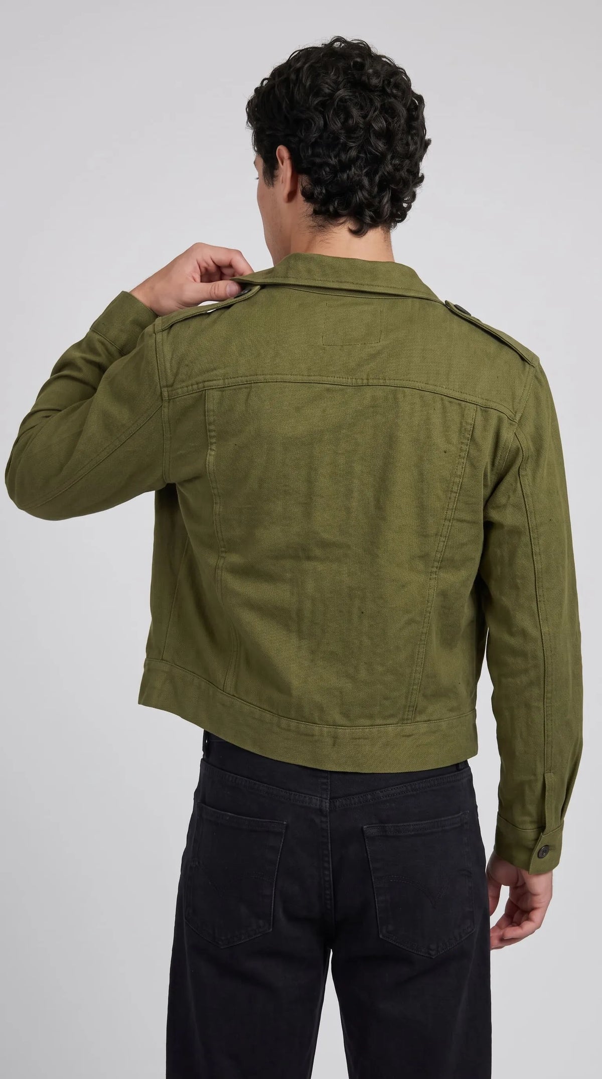 Olive drab cotton canvas Ike jacket showcasing its structured shoulder yoke, clean horizontal back seam, buttoned shoulder straps and wide straight hem, combining military heritage construction with a neat cropped silhouette for everyday layering.