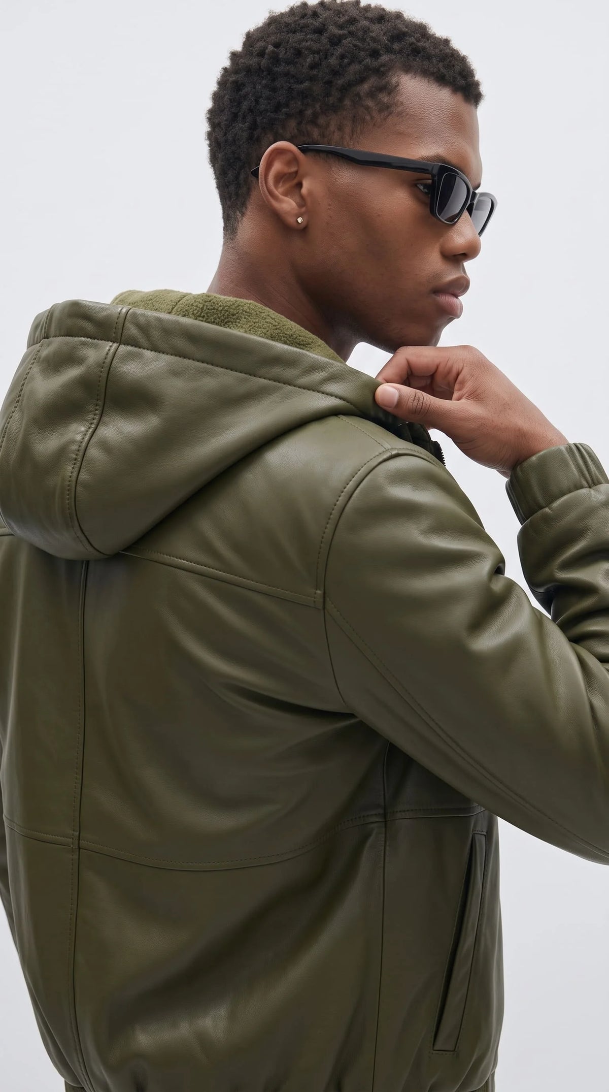 Close-up of an olive green pebbled leather bomber jacket highlighting its sculpted hood, soft matching faux-shearling interior, reinforced shoulder seams and smooth leather finish for a refined cold-weather outerwear design.