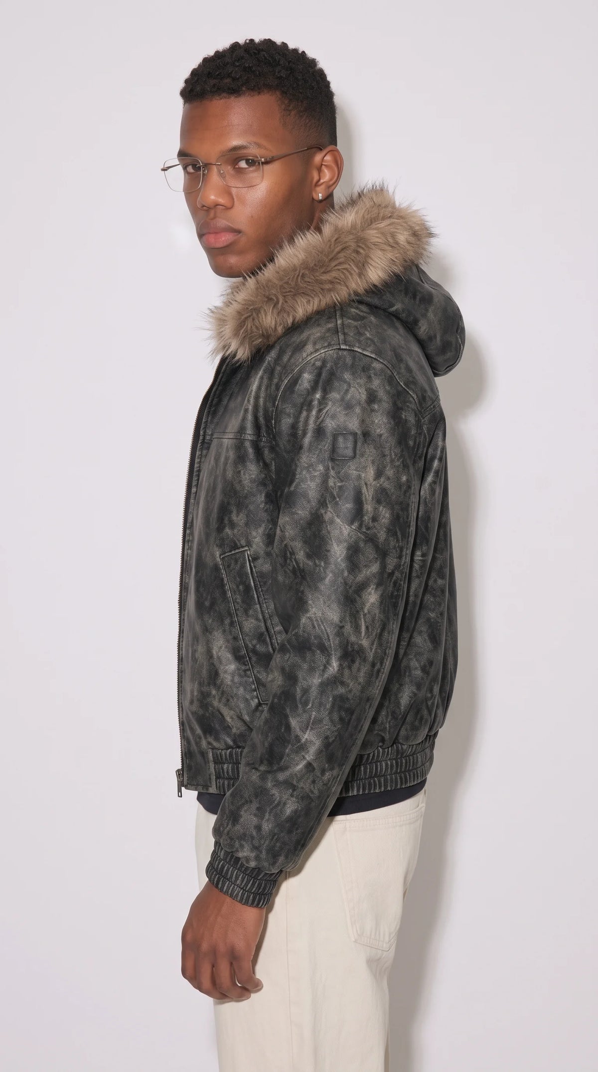 Oversized charcoal distressed leather bomber jacket featuring a fixed hood with earthy brown faux-fur trim, a sleeve utility patch, angled side-entry pockets and elasticated cuffs for a bold urban Y2K outfit.
